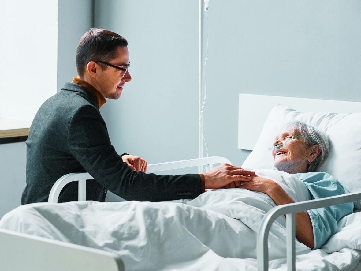 Ein Mann spricht zu einer kranken Frau, im Krankenbett