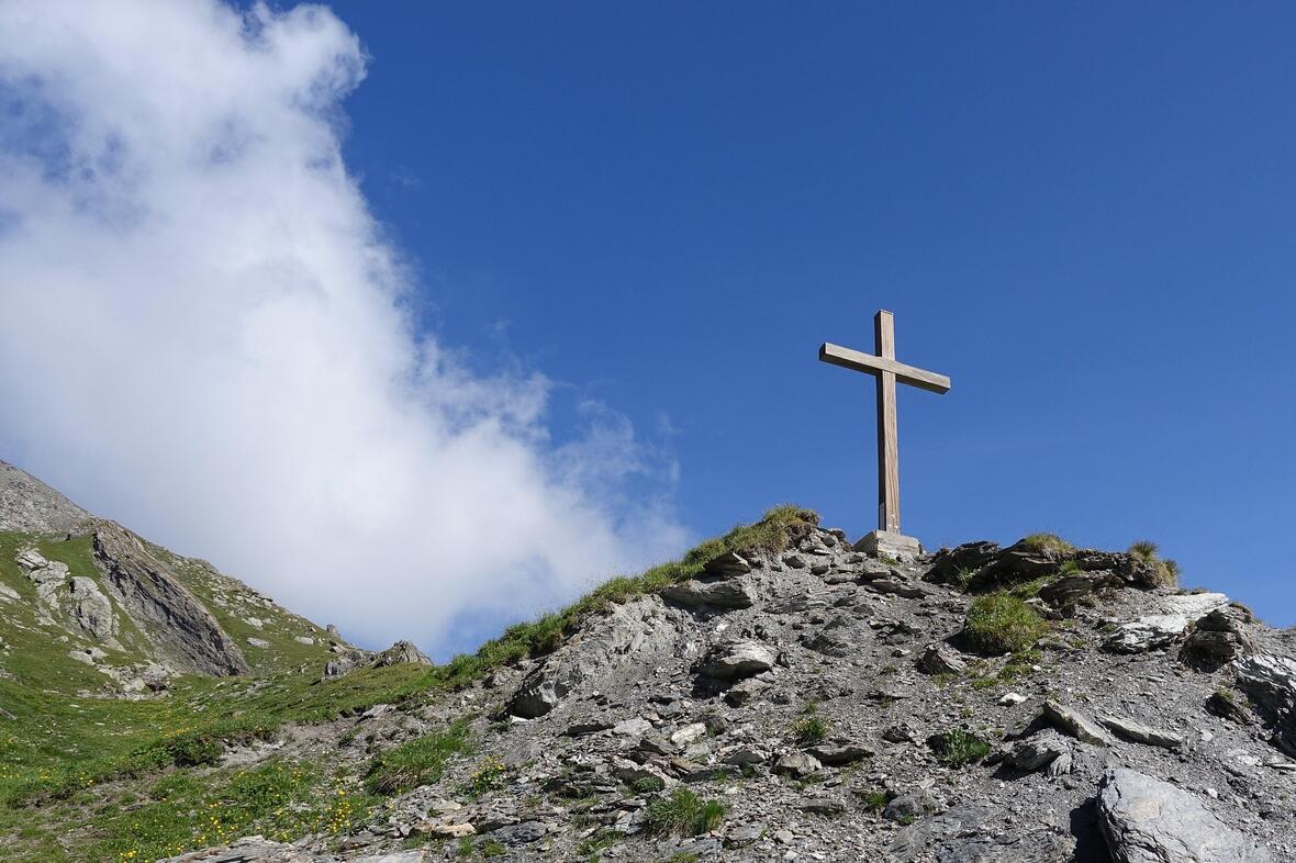 Die Berge im Fokus mit blauem Himmel, darauf ein Gipfelkreuz