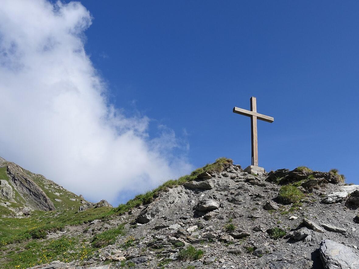 Die Berge im Fokus mit blauem Himmel, darauf ein Gipfelkreuz